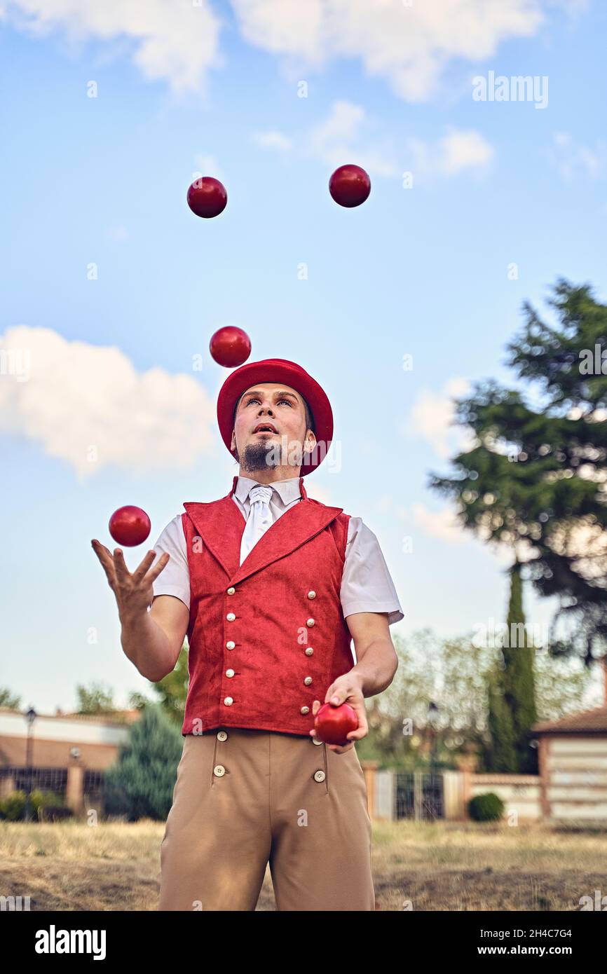 From below bearded male juggler in costume juggling red balls during performance on sunny summer day in park Stock Photo