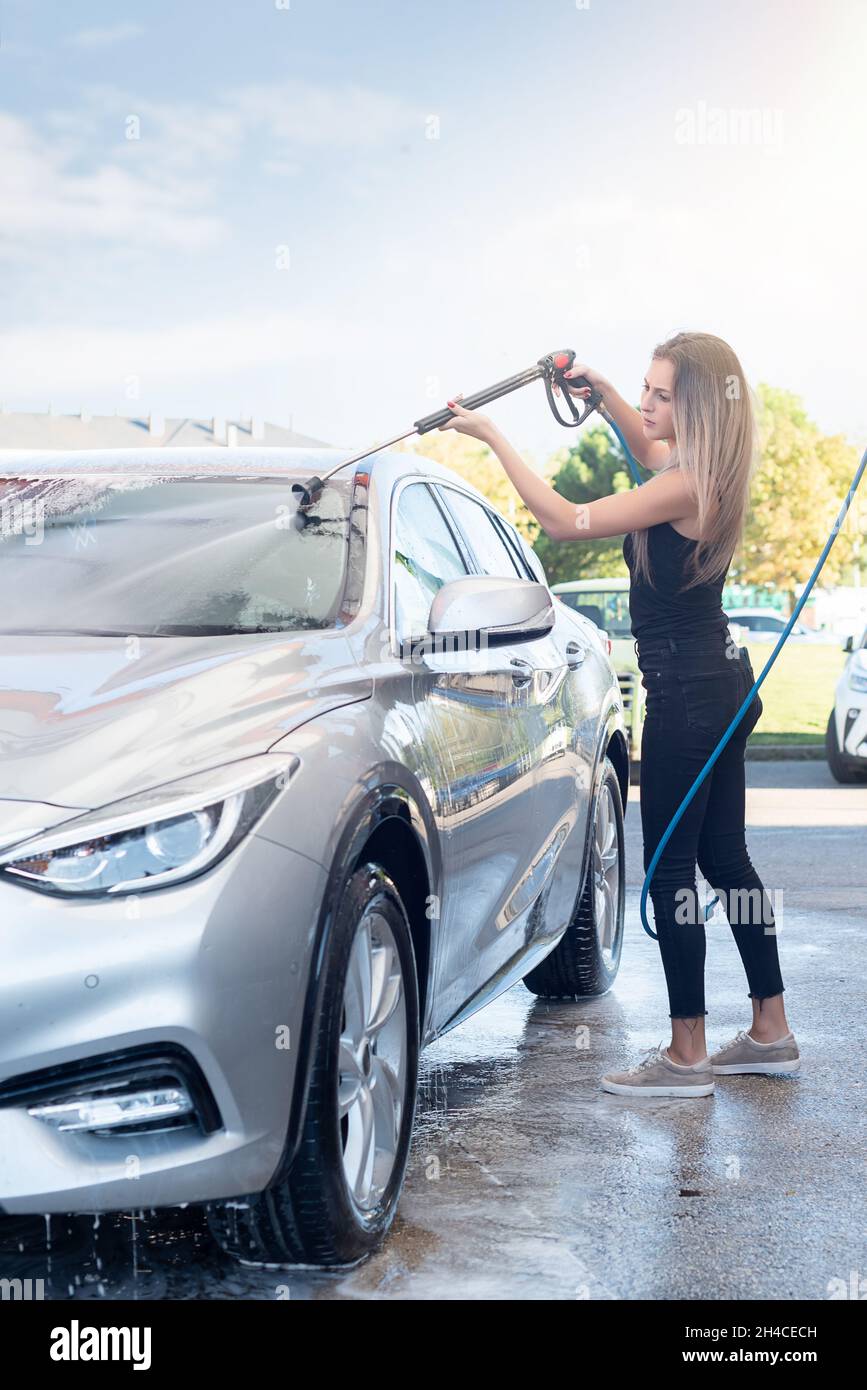 Cute blonde woman in jeans and black t-shirt washing the car Stock Photo