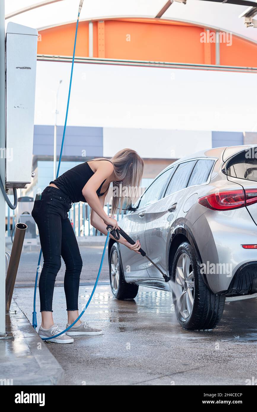 Cute blonde woman in jeans and black t-shirt washing the car Stock Photo