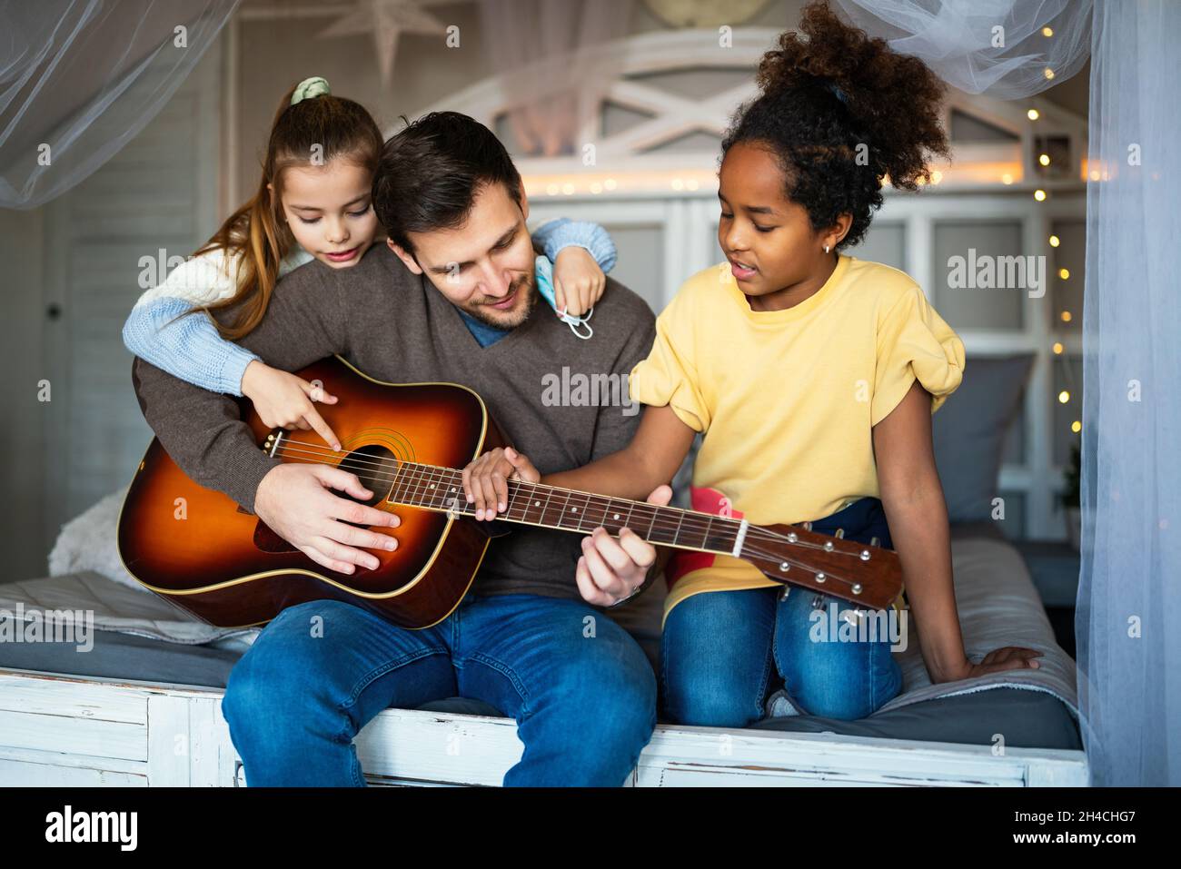 Smiling father with multiethnic children having fun and playing guitar at home Stock Photo