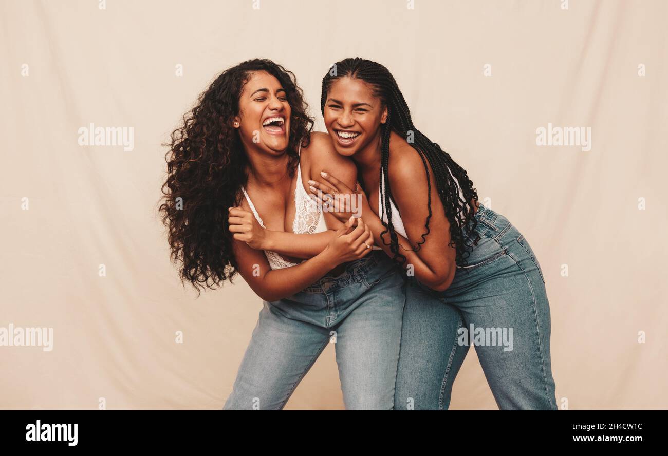 Fun with bestie. Two happy young women laughing and being playful while wearing denim jeans against a studio background. Two cheerful female friends b Stock Photo