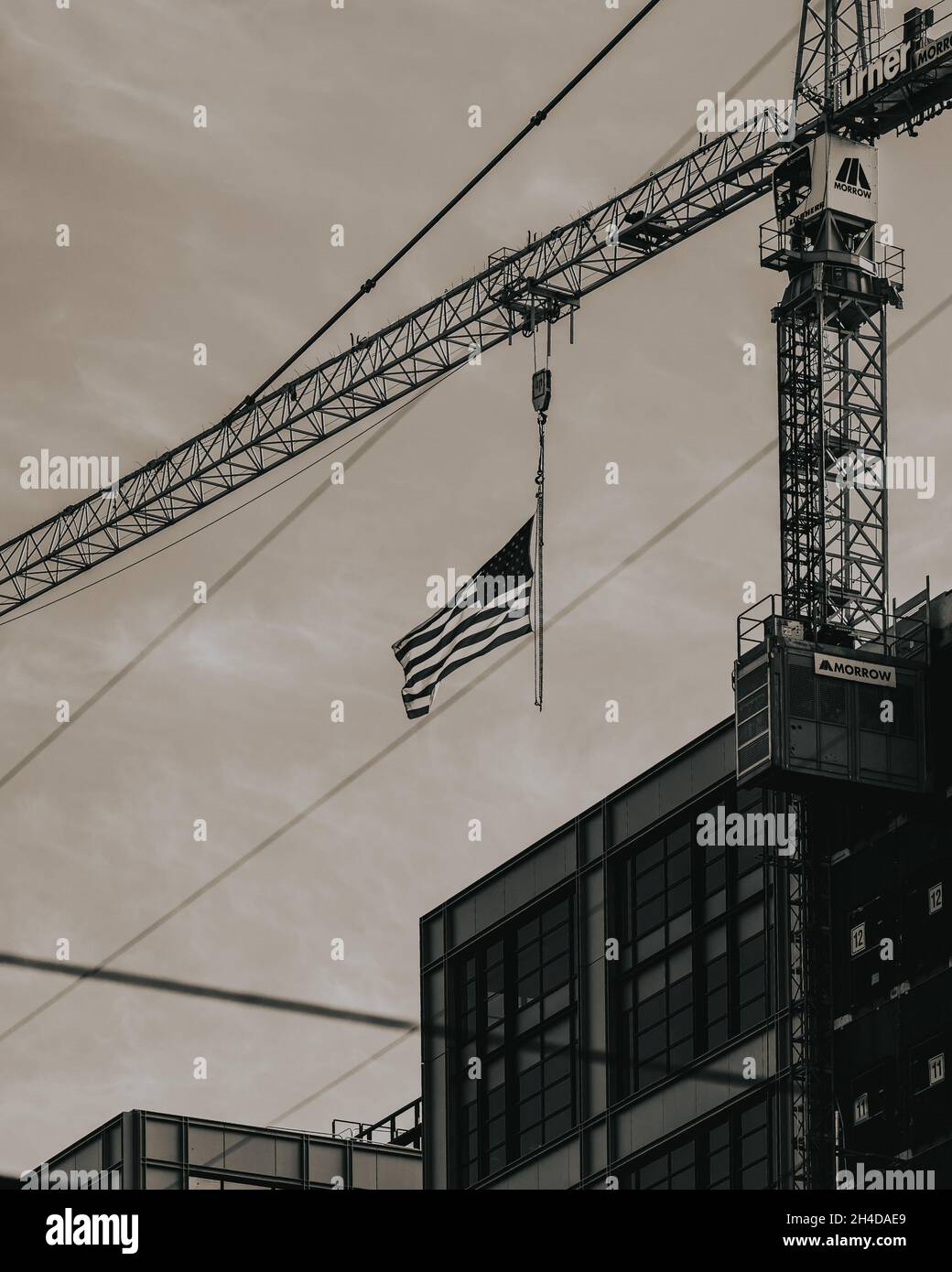 Vertical grayscale shot of an American flag hanging from crane Stock Photo