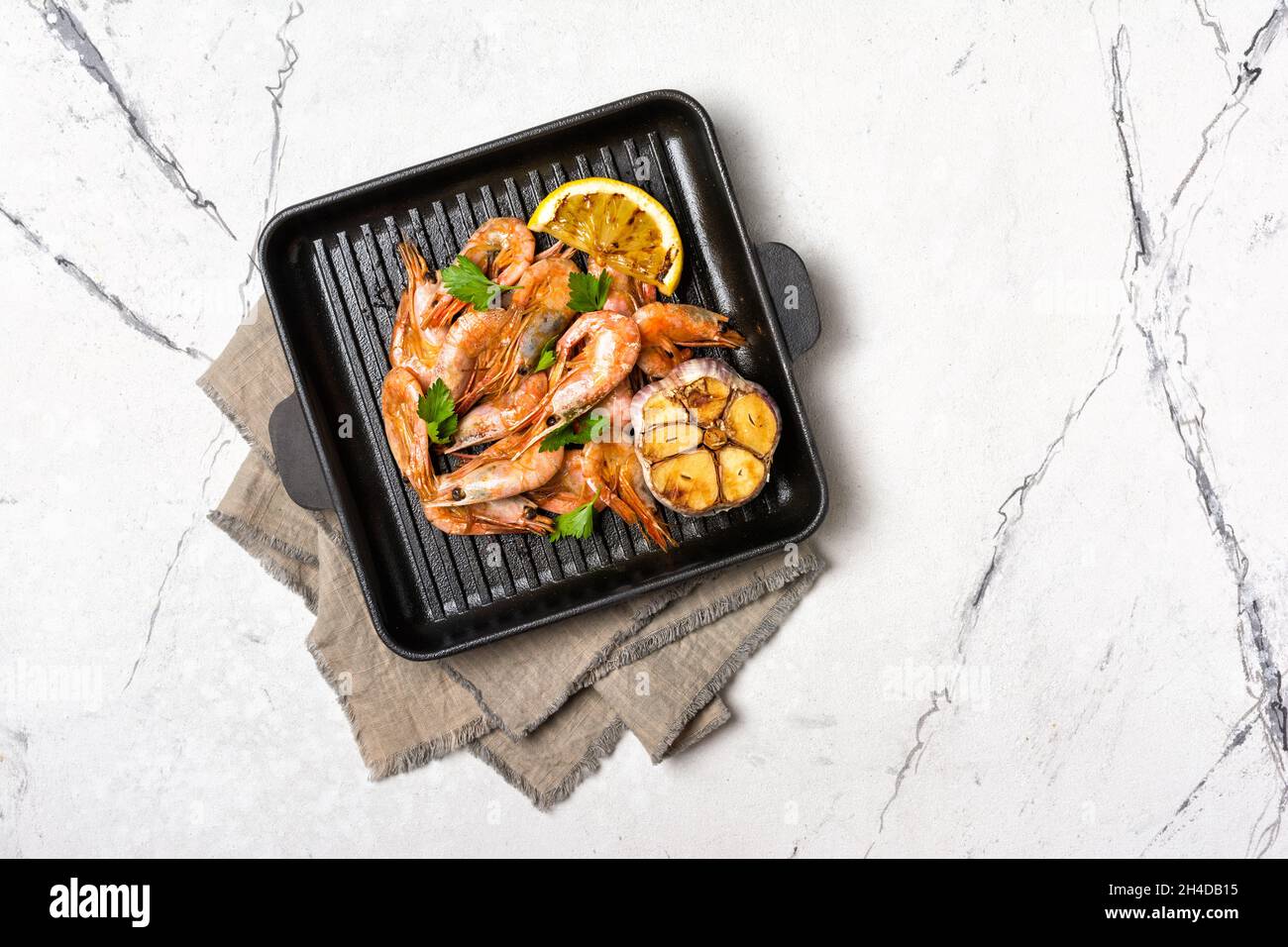 Top view of grilled shrimps on cast iron skillet or pan with spice, fried lemon and garlic on white marble background Stock Photo