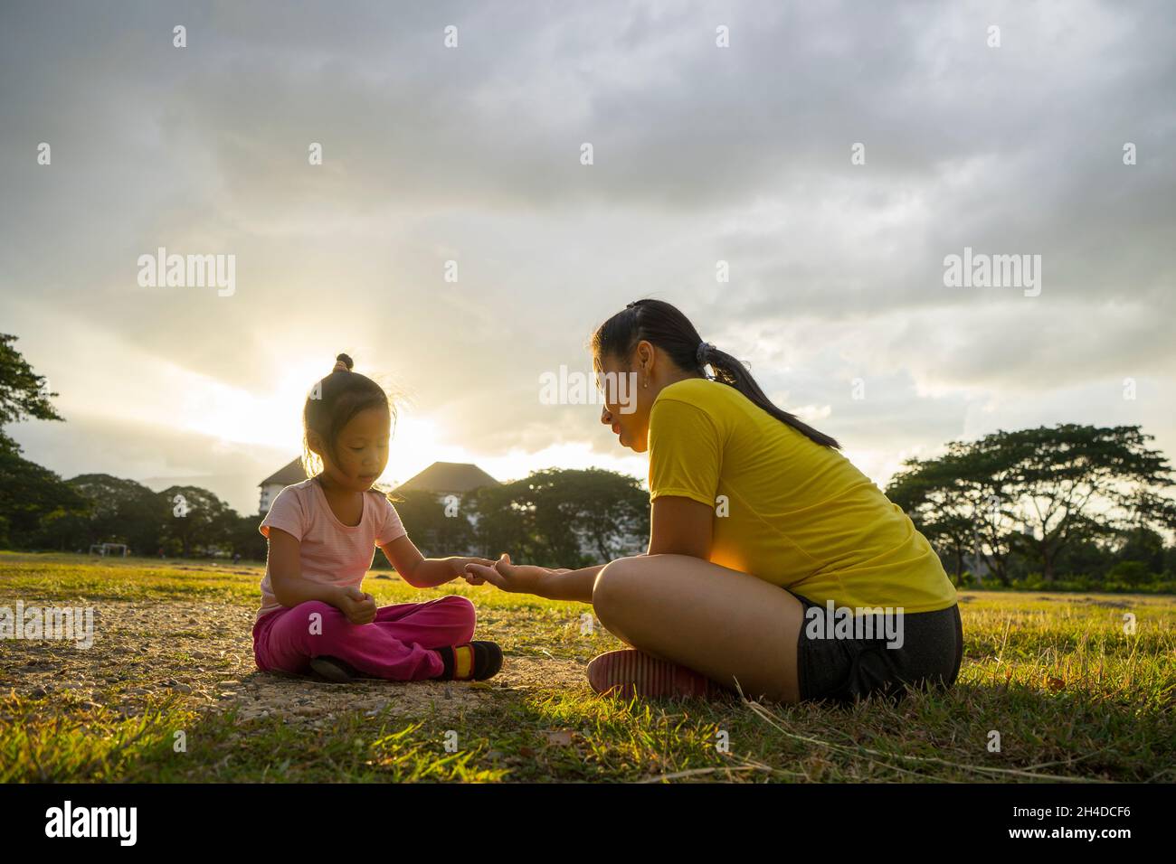 Mother and daughter playing on the green football field at the sunset time. Concept of friendly family. Stock Photo