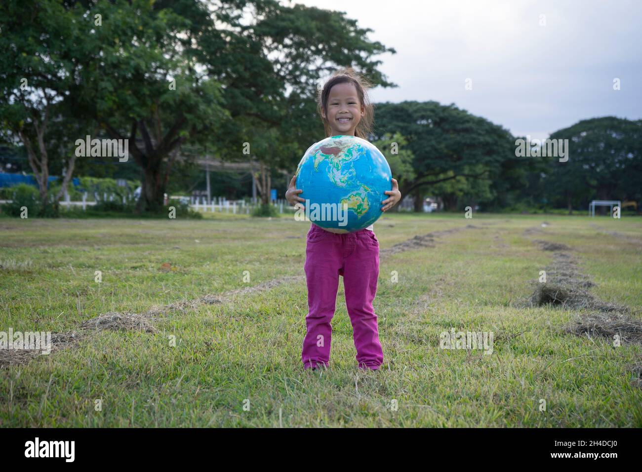 Smiling little asian girl holding an earth globe in the park on a sunny day, Earth day holiday concept. Protection and love of earth Stock Photo