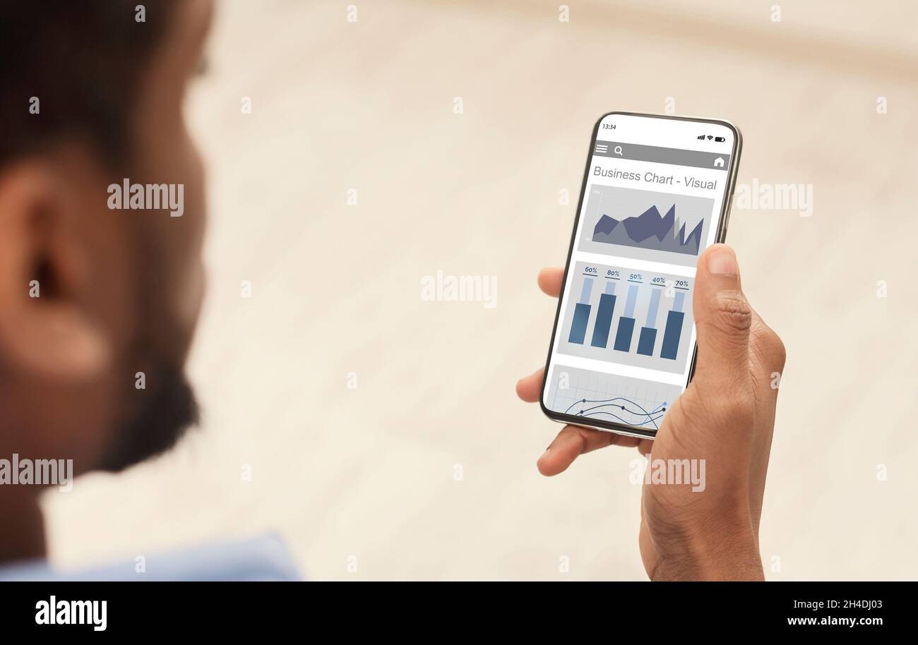 Millennial black guy with beard uses website or app with financial profit charts on smartphone screen Stock Photo