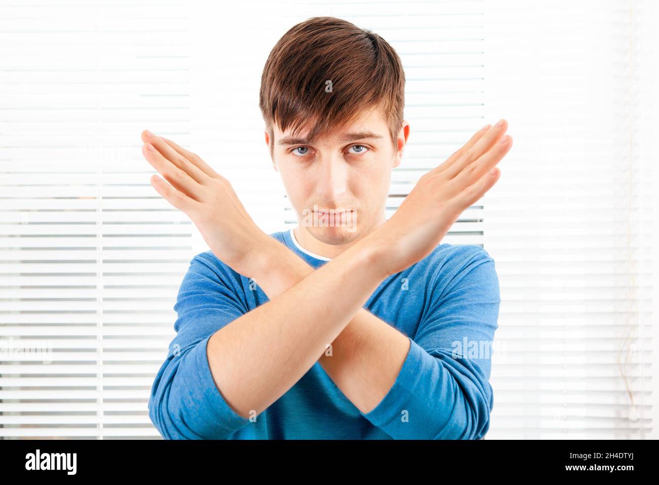 Serious Young Man show a Refusal Gesture on the Jalousie Background in a Room Stock Photo