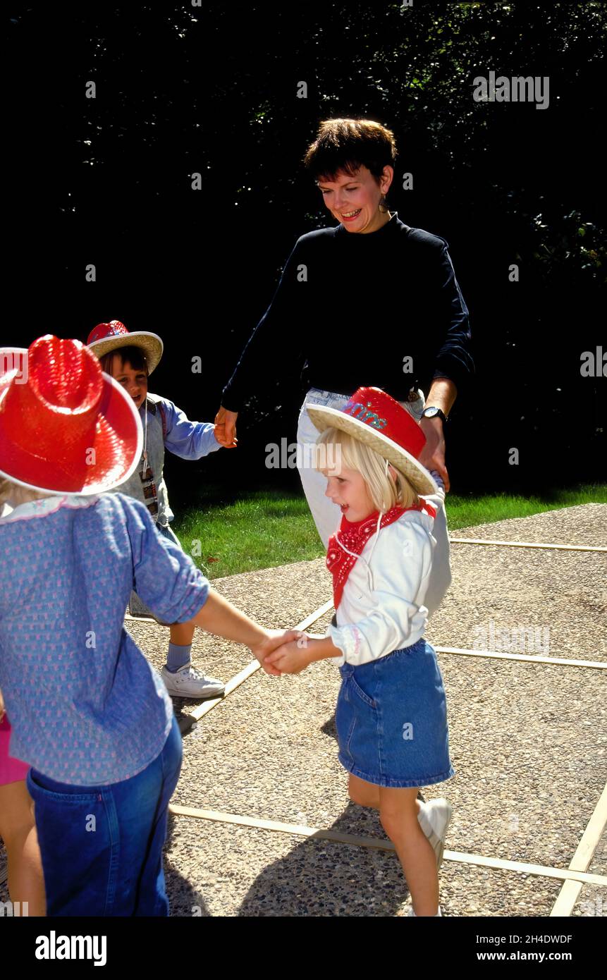 A mother plays with children dancing and holding hands in a circle at a birthday party. Stock Photo