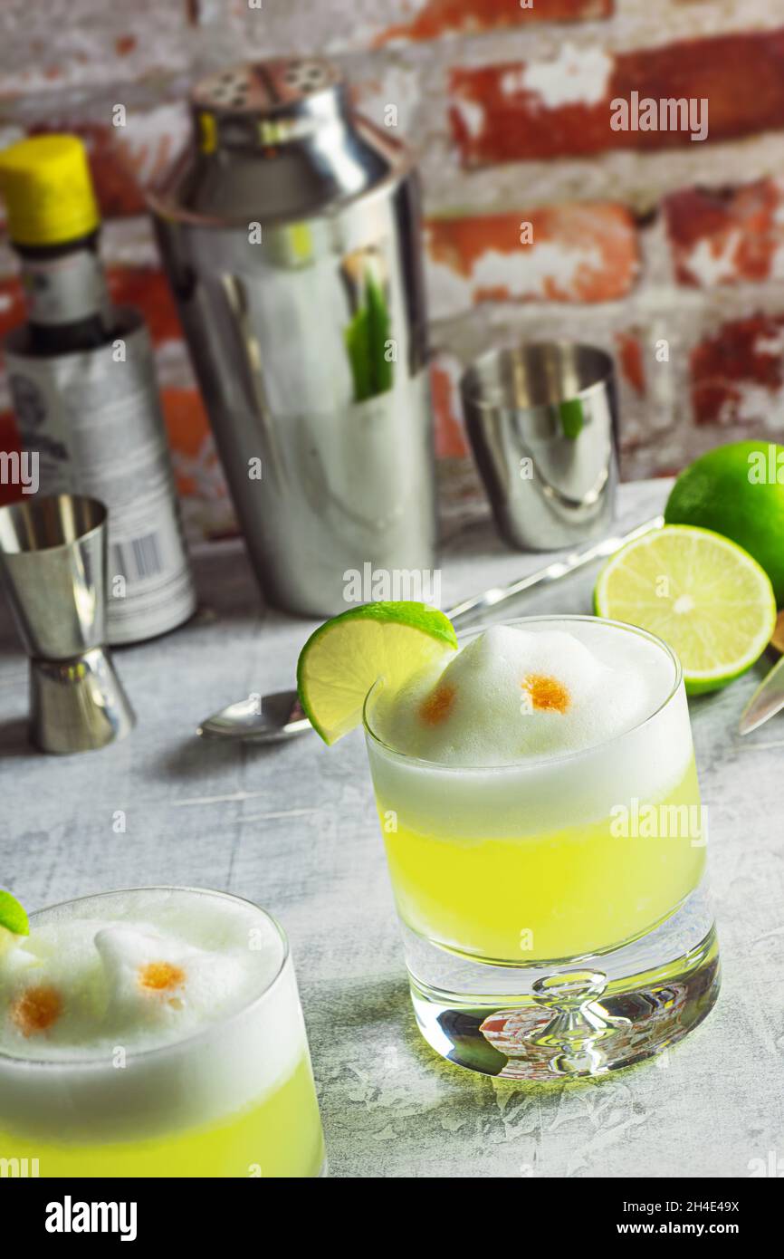 Pisco Sour Cocktails with Lime and Egg White Foam on Bar Top with Tools Stock Photo