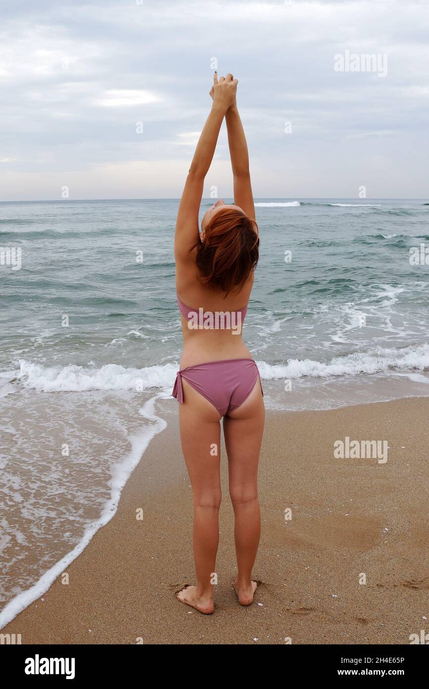 teenage girl stands in a swimsuit on the seashore raising her hands up, back  view Stock Photo - Alamy