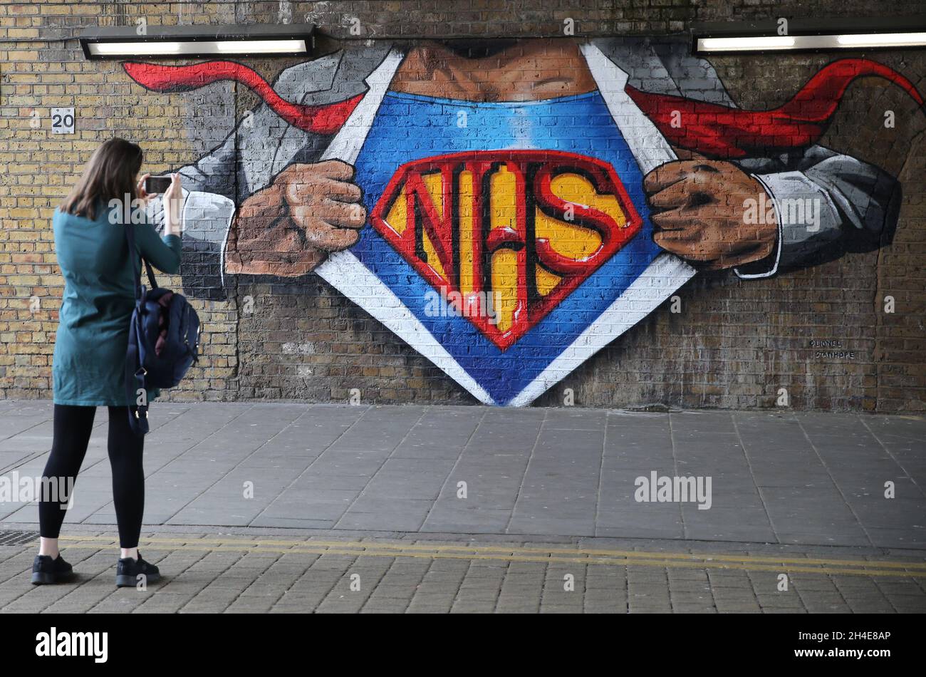 A woman takes a picture of a NHS superman graffiti by street artist Lionel Stanhope to pay tribute to NHS workers by Waterloo, London, as the UK continues in lockdown to help curb the spread of the coronavirus. Picture date: Friday May 8, 2020. Stock Photo
