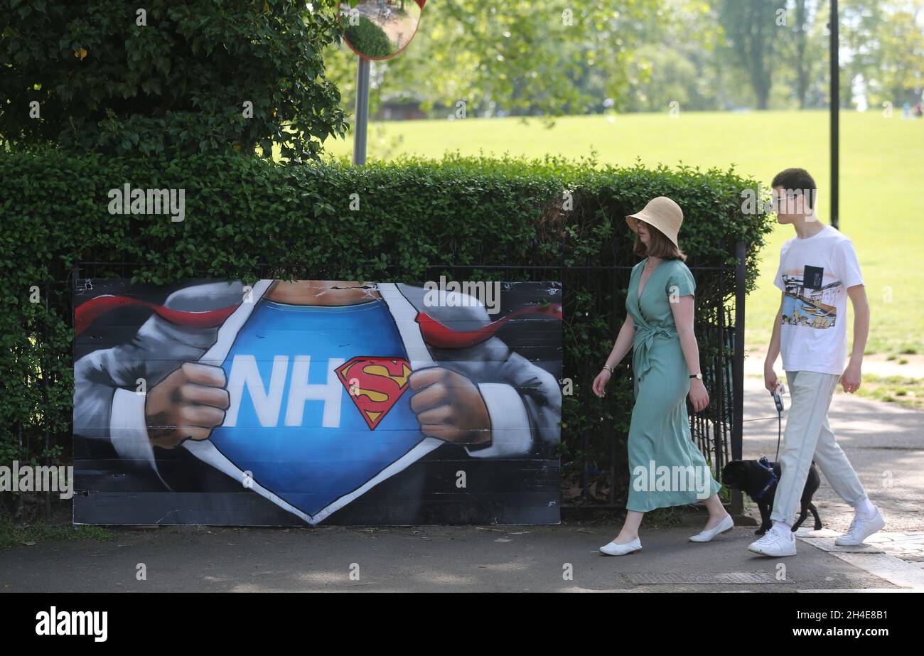 People walk past a NHS superman graffiti by street artist Lionel Stanhope to pay tribute to NHS workers by Ladywell, south east London, as the UK continues in lockdown to help curb the spread of the coronavirus. Picture date: Friday May 8, 2020. Stock Photo