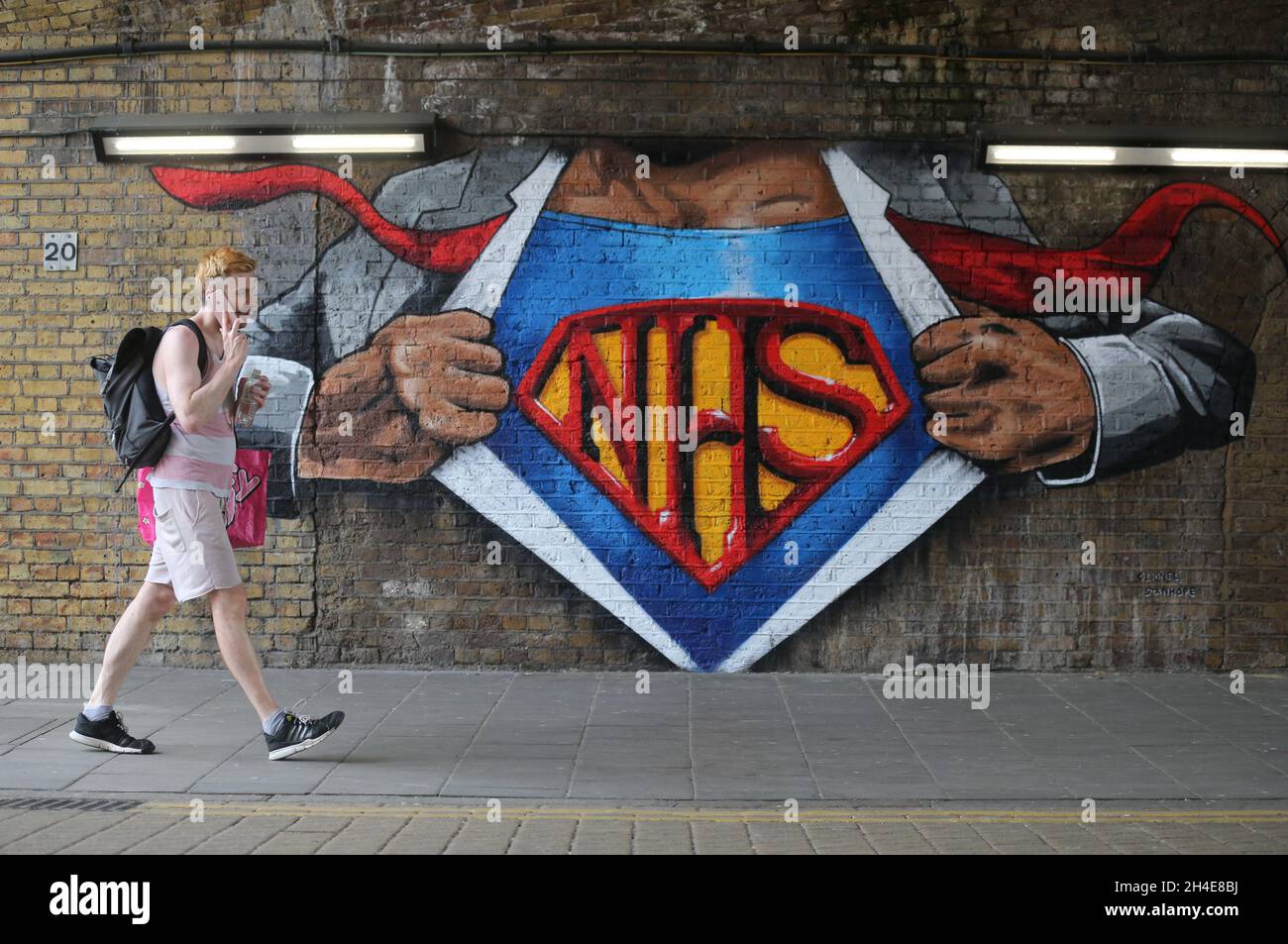 A man walks past of a NHS superman graffiti by street artist Lionel Stanhope to pay tribute to NHS workers by Waterloo, London, as the UK continues in lockdown to help curb the spread of the coronavirus. Picture date: Friday May 8, 2020. Stock Photo
