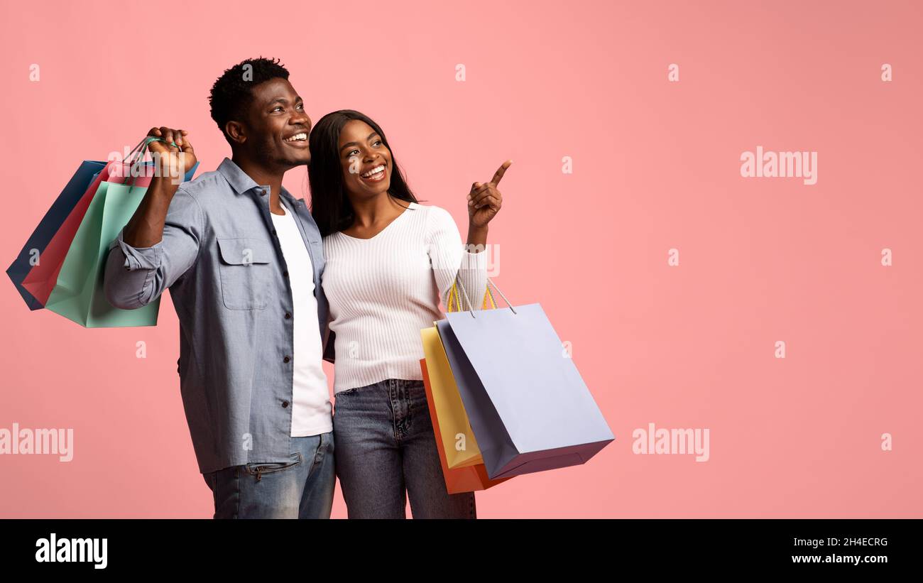 Positive african american lovers with purchases pointing at copy space Stock Photo