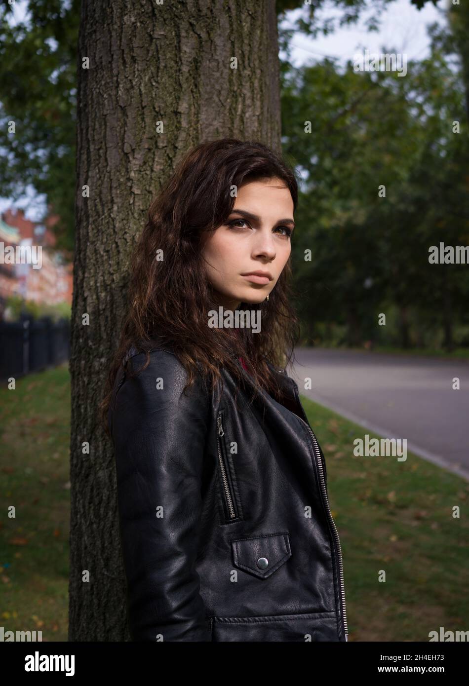 Portrait of a young woman in a black leather jacket standing in front ...