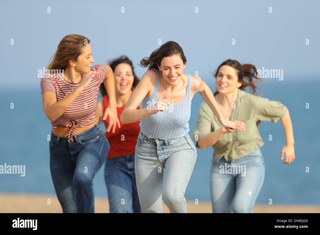 Front view portrait of four excited friends running and joking on the beach Stock Photo