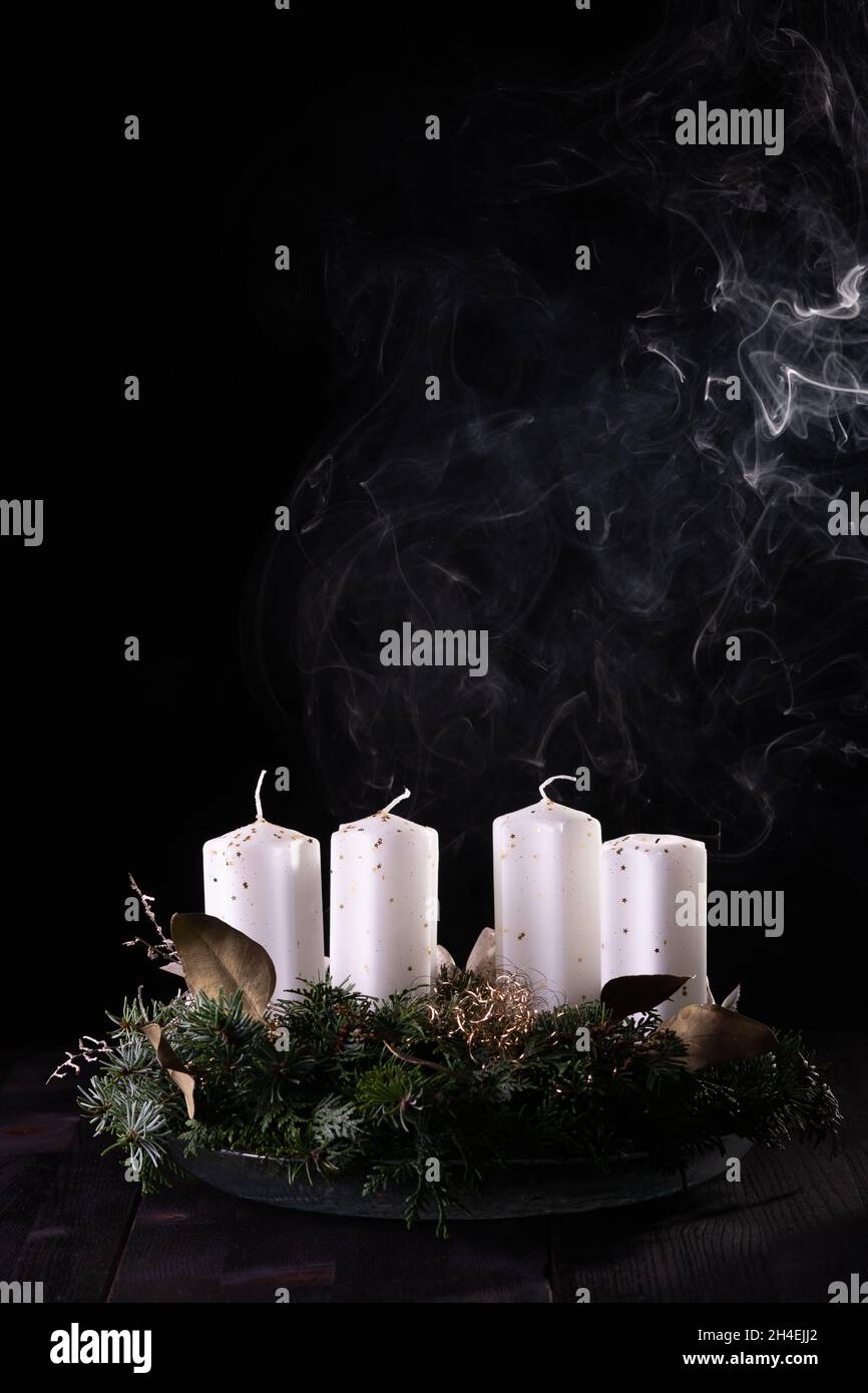 First Advent - Advent wreath from fir and evergreen branches with blown out candle on dark wooden table. White smoke on black background, copy space. Stock Photo
