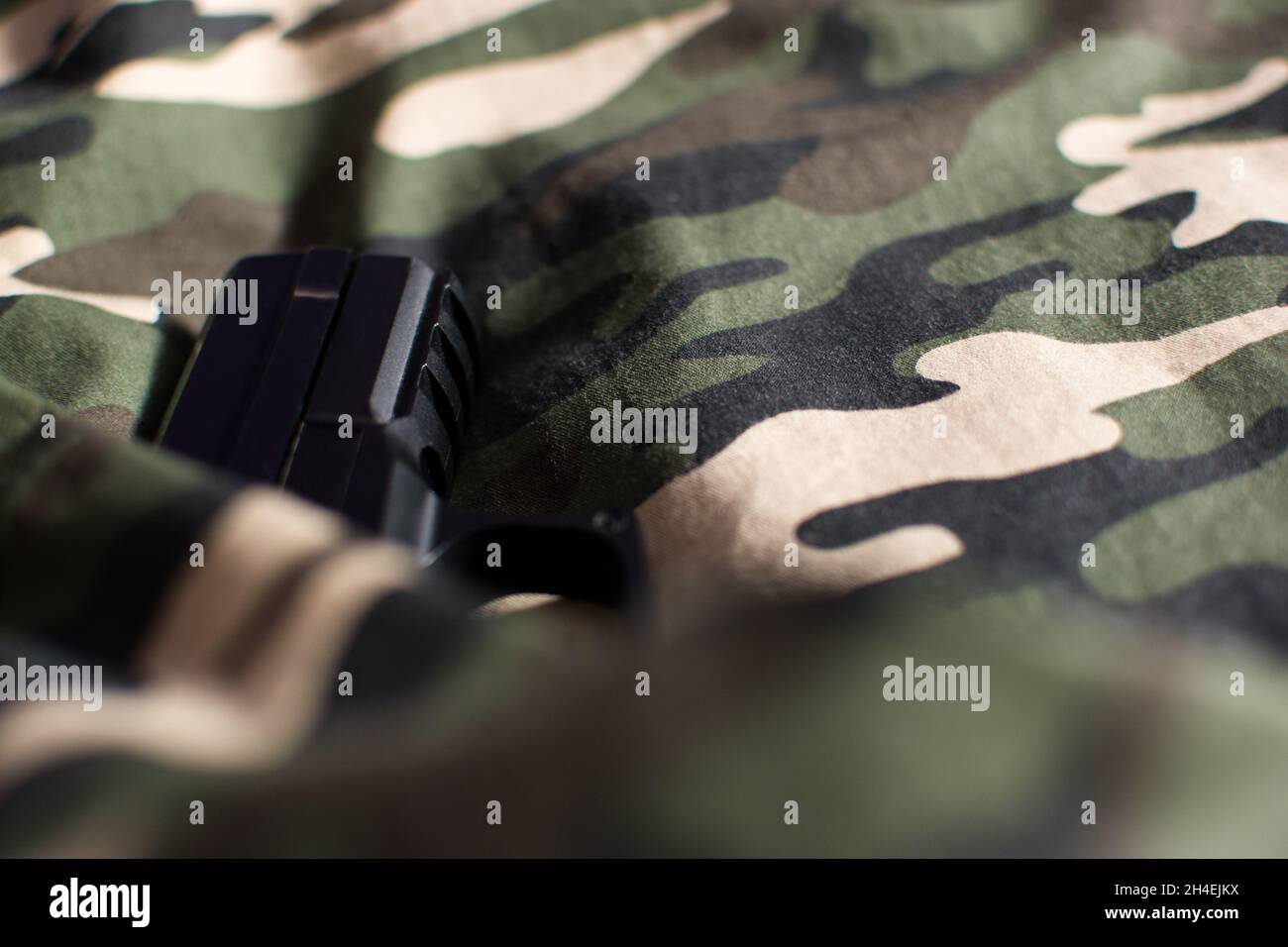 Black handgun, pistol wrapped in camouflage military uniform, copy space Stock Photo