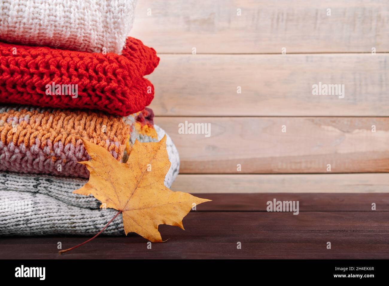 Stack of warm knitted sweaters. Autumn concept. Woolen jumpers and maple leaf on a wooden background. Stock Photo