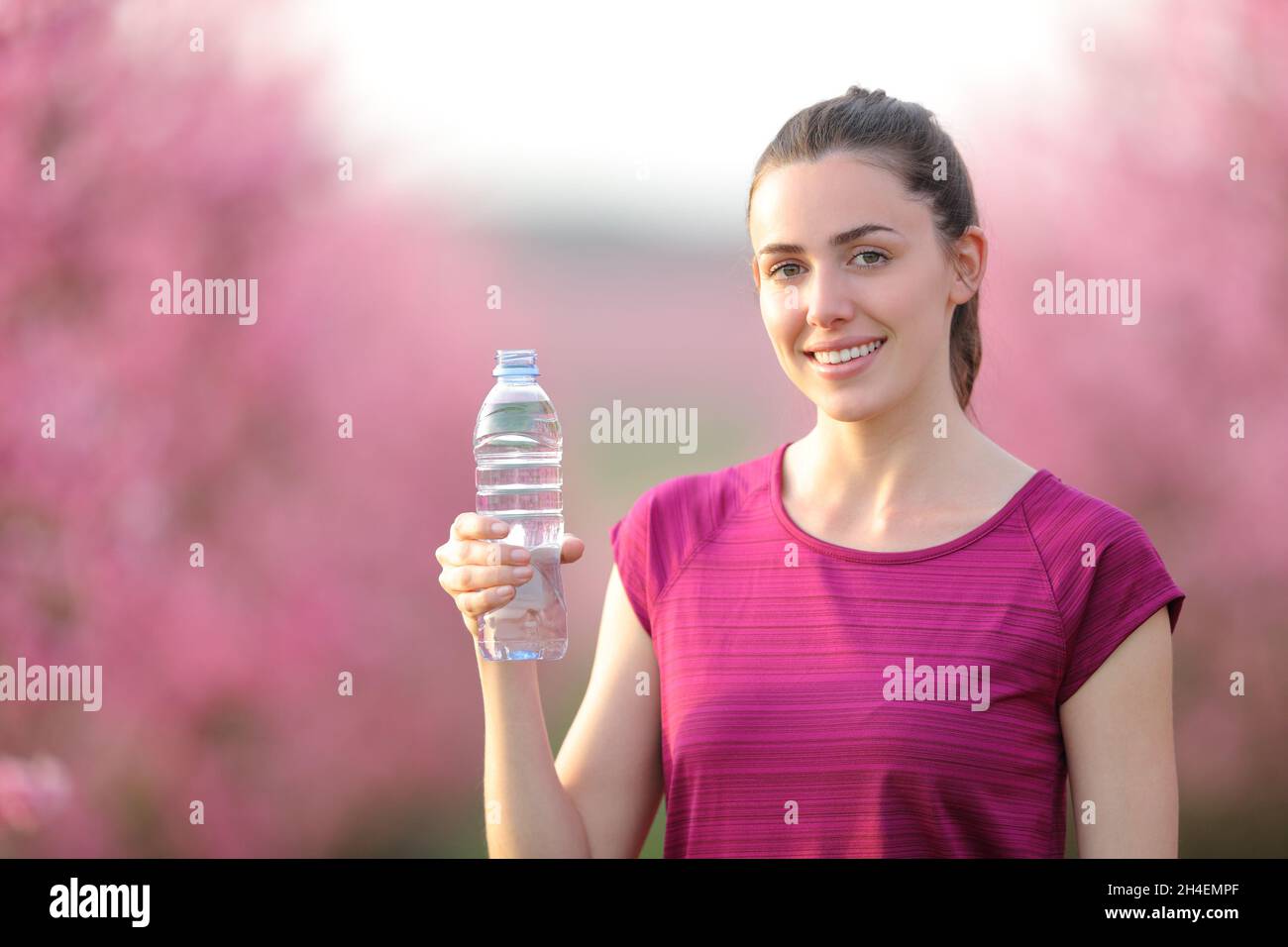 Happy sportswoman holding water bottle looking at you standing in a ...