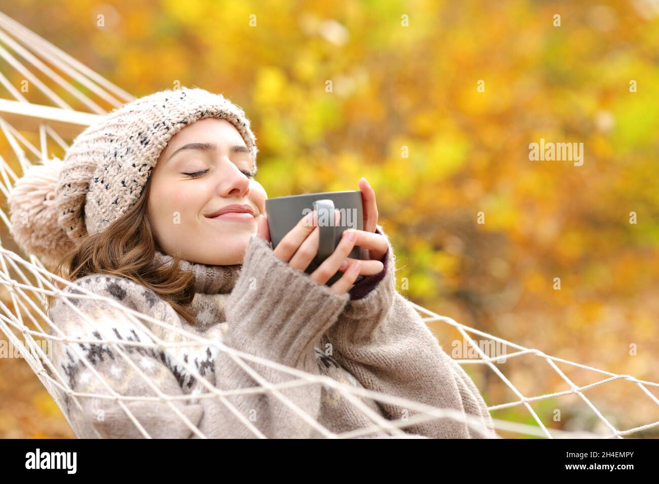 Happy woman holding coffee mug lying on hammock in autumn in a forest Stock Photo
