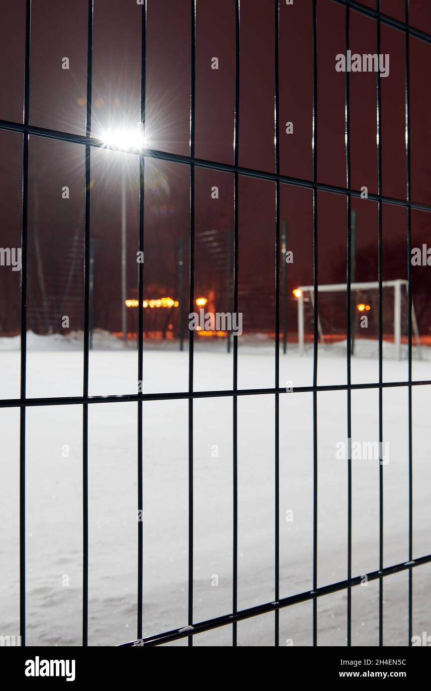 Soccer football field covered with a thick layer of snow. View through the fence. Focus on the fence. Blurred photo. Night game is canceled Stock Photo