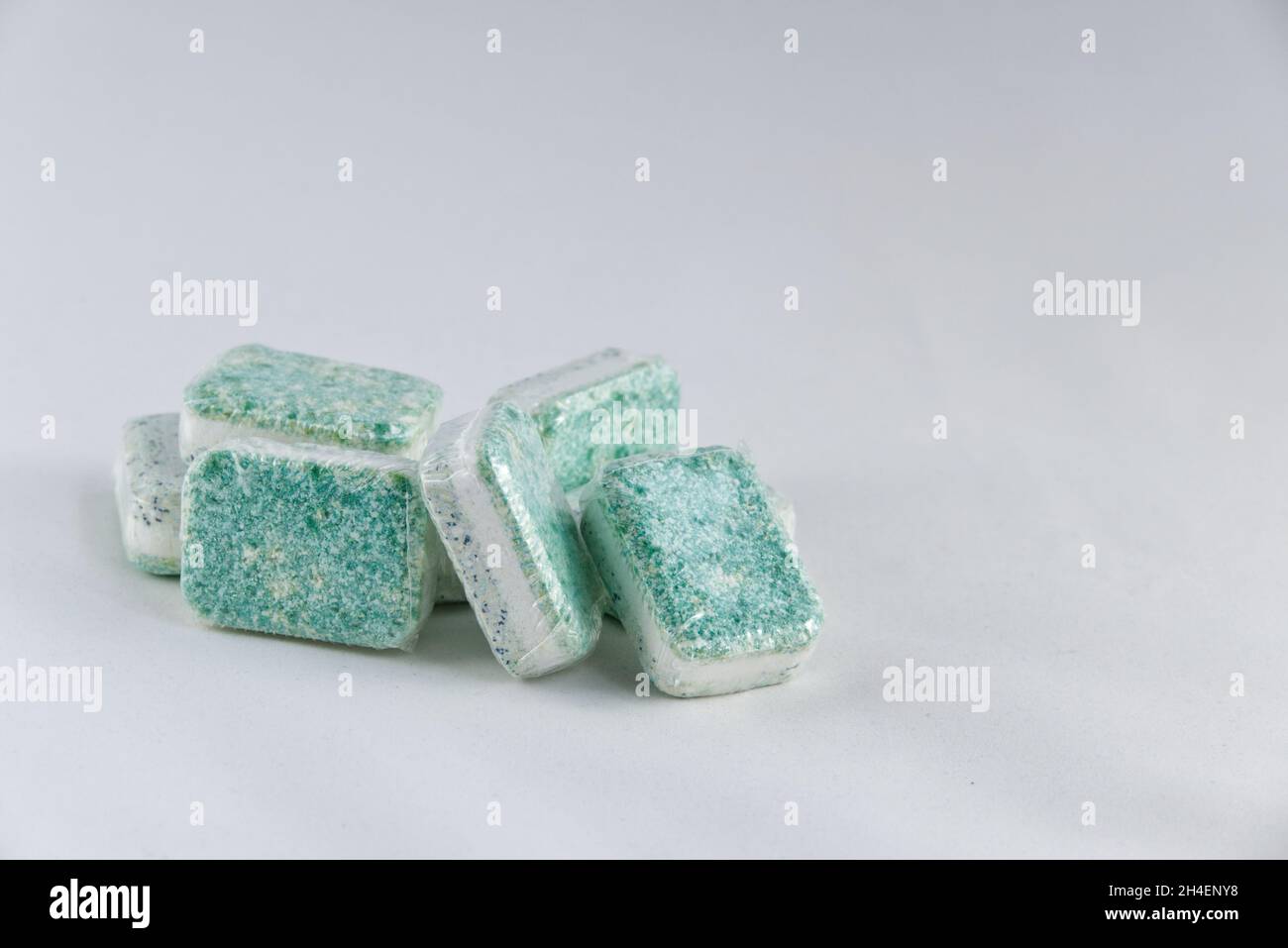A heap of dishwasher tablets, colored green and white, stacked randomly against a white background. Generic brand, wrapped in soluble plastic. Stock Photo