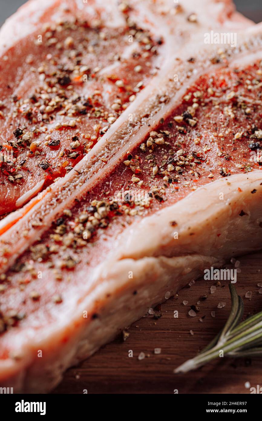 three lovely raw marbled black Angus beef steaks flavored with a mixture of ground pepper and ready to cook and serve on a dark wooden background. Stock Photo