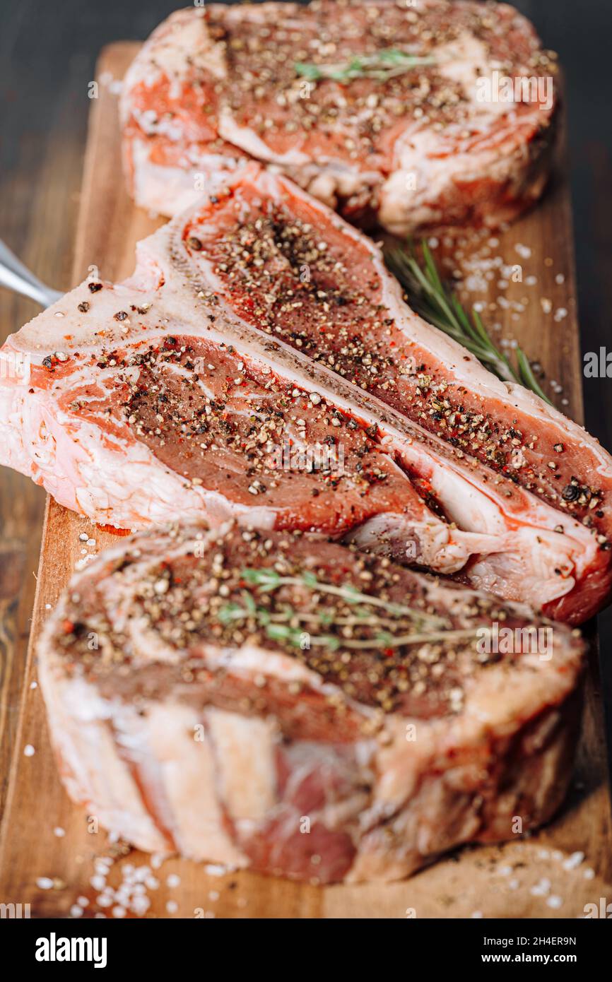 three lovely raw marbled black Angus beef steaks flavored with a mixture of ground pepper and ready to cook and serve on a dark wooden background. Stock Photo