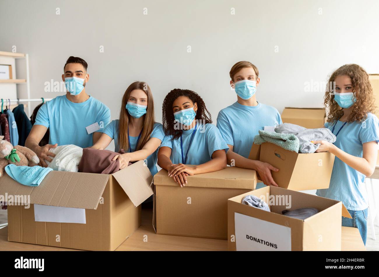 Homeless care concept. Young volunteers in medical face masks sorting clothing donations, working in charity center Stock Photo