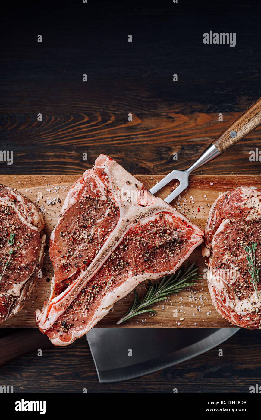 three lovely raw marbled black Angus beef steaks flavored with a mixture of ground pepper and ready to cook and serve on a dark wooden background. Stock Photo