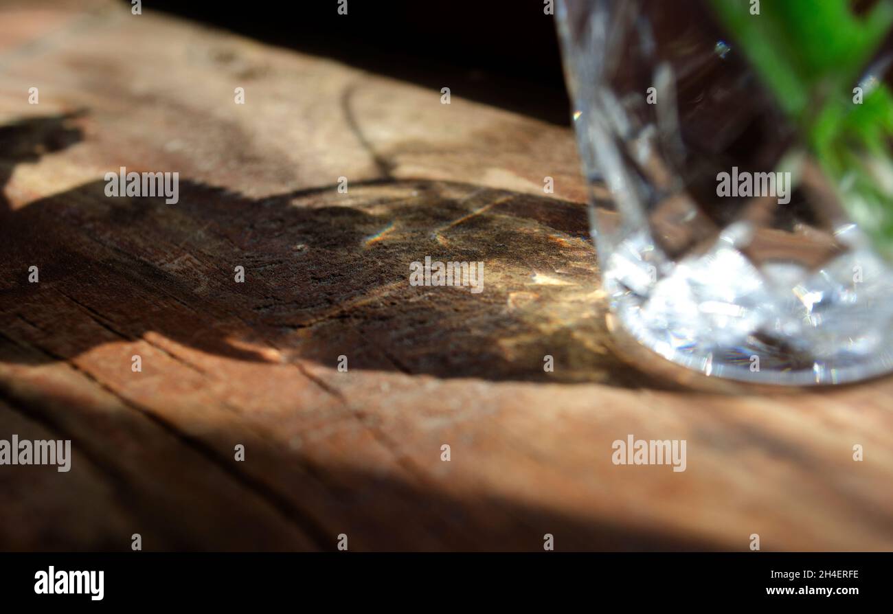 Water in glass with caustic light. Dispersion light. Crystal light and shadow on wooden surface. Stock Photo