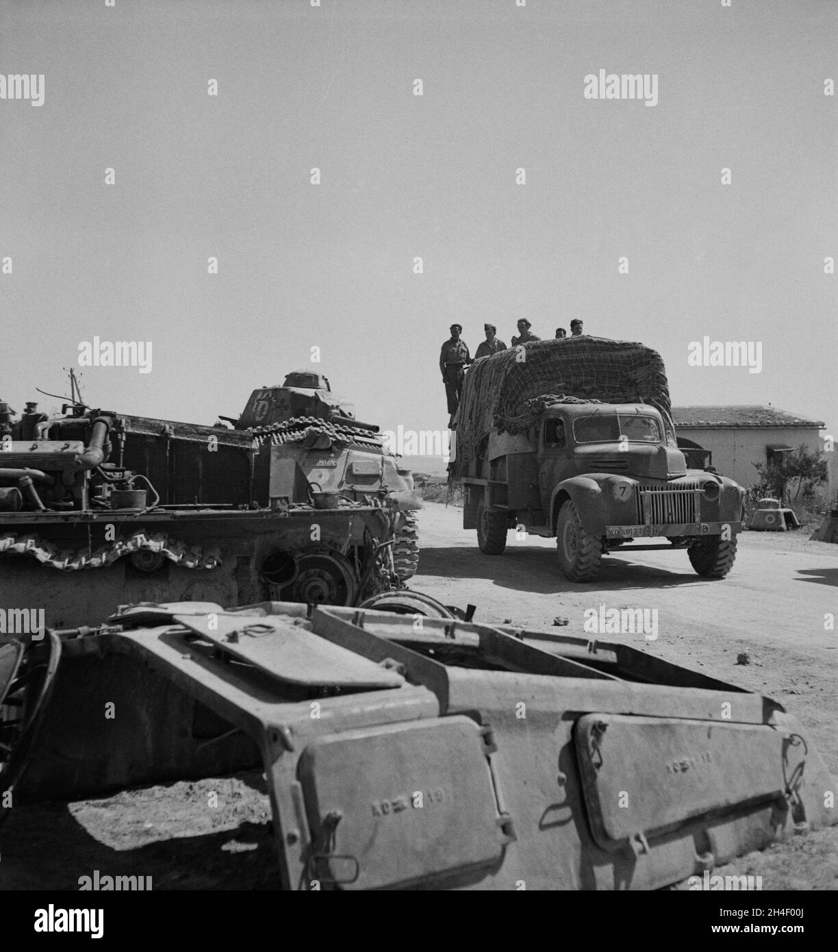 A vintage photo circa May 1943 an allied truck filled with British soldiers of the 8th army passes wrecked German tanks in Porto Farina, Tunisia during World War 2.  Taken at the end of the Battle of Tunis when the Afrika Korps finally surrendered to the allies. Stock Photo