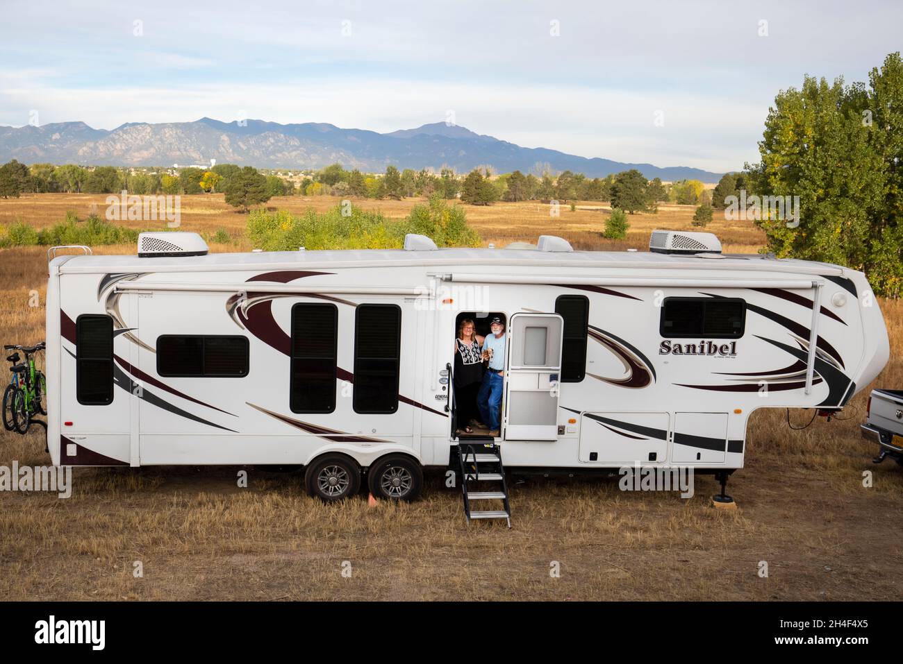 Retired travelers with their dog stand on the steps of their Recreational vehicle with Colorado mountains in the background. RV Stock Photo