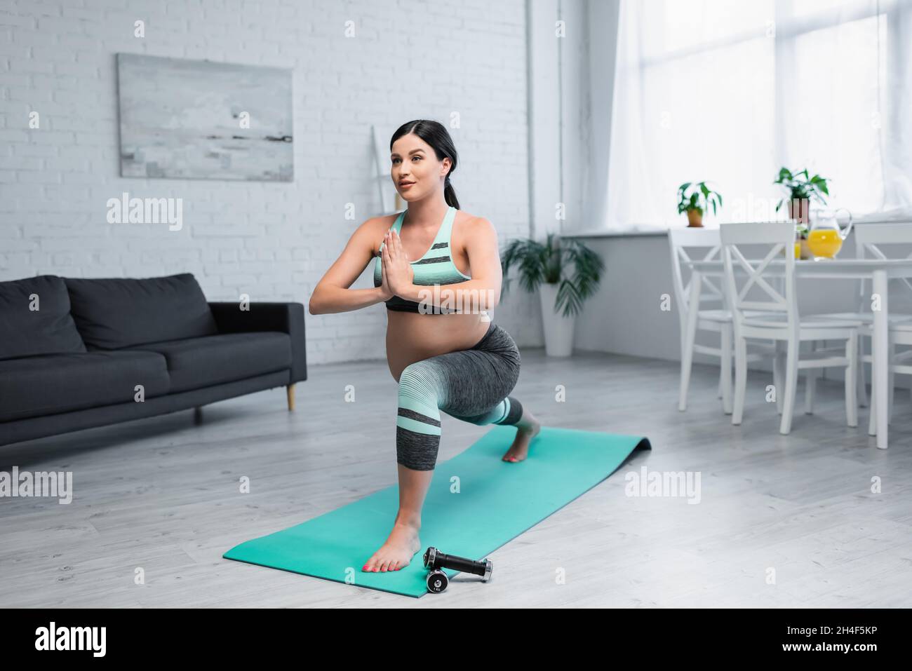 pregnant woman practicing crescent lunge pose with praying hands in ...