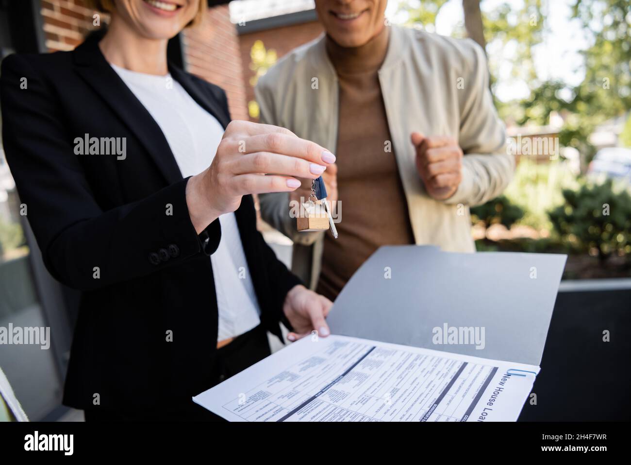 partial view of cheerful realtor holding key near blurred and happy man ...