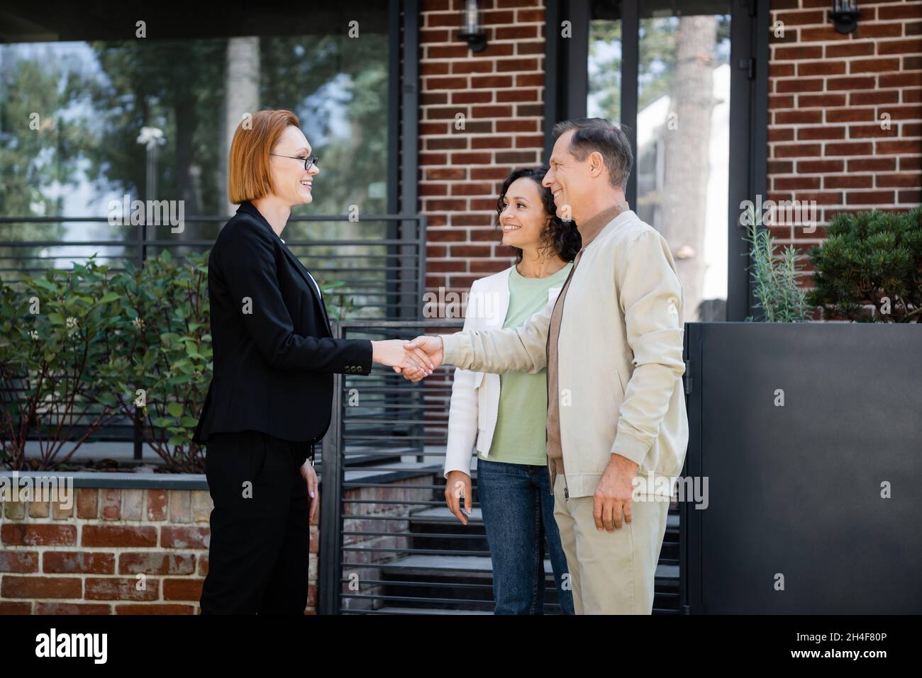 happy realtor in glasses shaking hands with man standing near african ...
