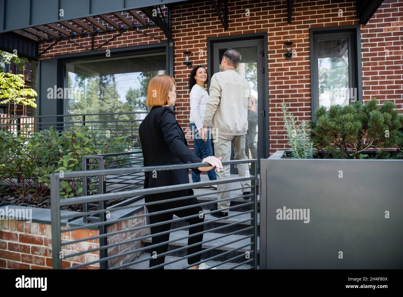 Redhead Realtor Standing Behind Interracial Couple Near Modern House