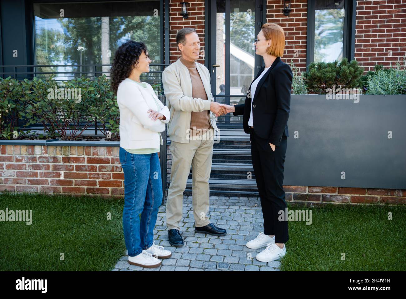 happy realtor in glasses shaking hands with smiling man standing near ...