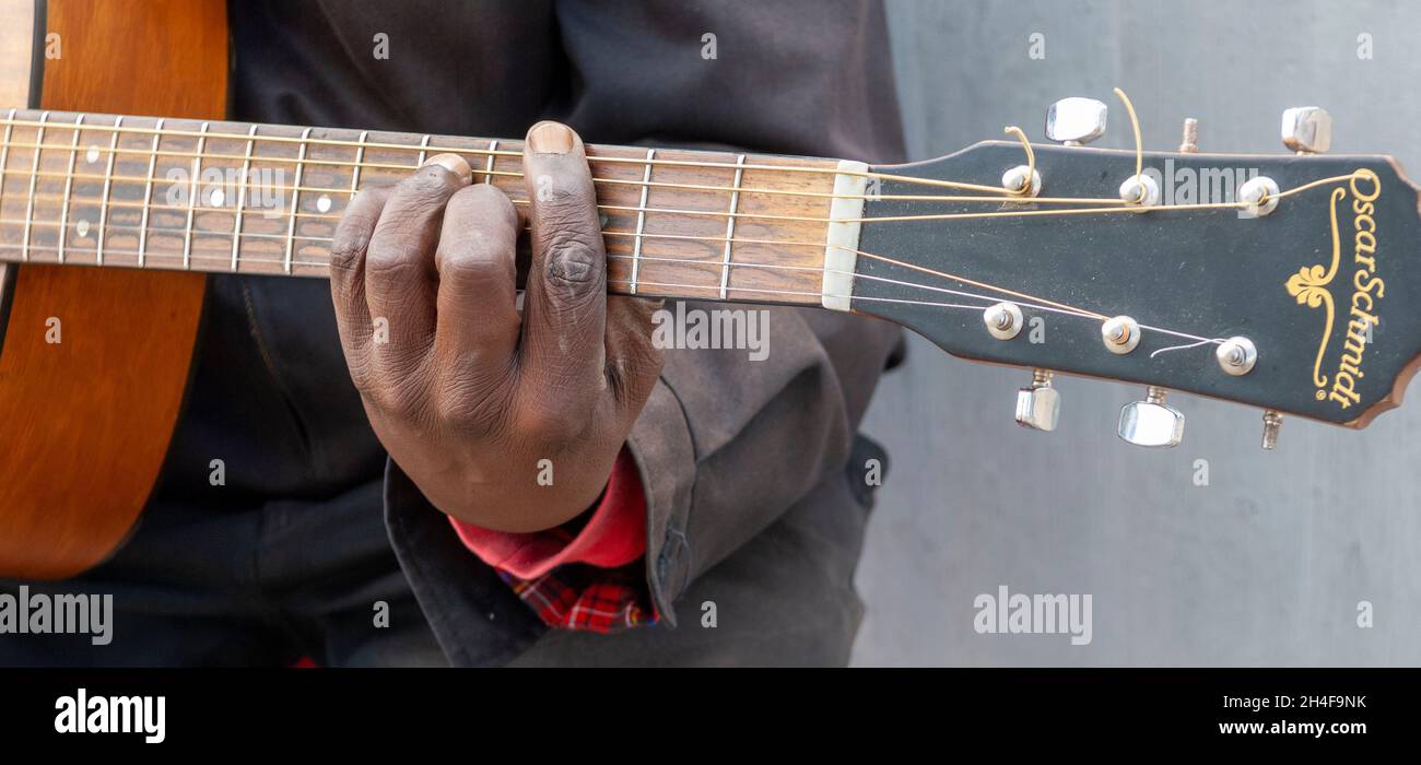 A black mans hand on the fingerboard - fretboard of an acoustic guitar playing in a public situation, Cape Town, South Africa. Stock Photo