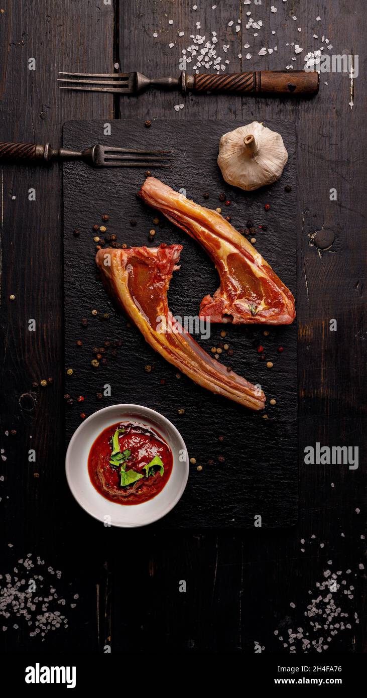 Raw lamb ribs. Halal mutton meat. Lamb rack on a dark background. Salt, spices, garlic, sauce and forks. Top view. Vertical shot. Copy space Stock Photo