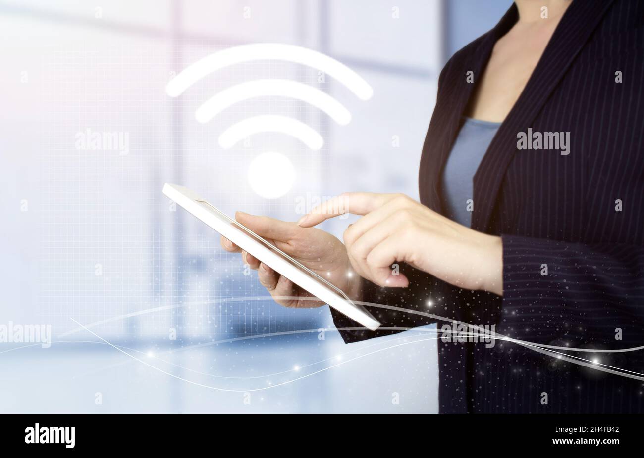 Wi Fi wireless concept. Hand touch white tablet with digital hologram Wi Fi sign on light blurred background. Business networking connection concept a Stock Photo