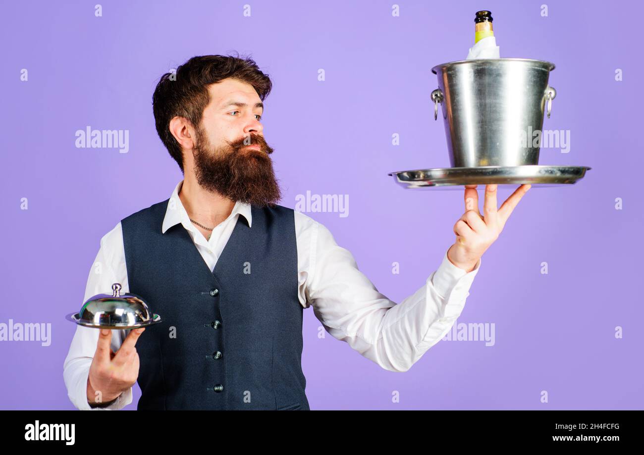 Professional waiter in uniform with serving tray and wine cooler. Restaurant serving. Butler carrying restaurant cloche and ice bucket with bottle Stock Photo