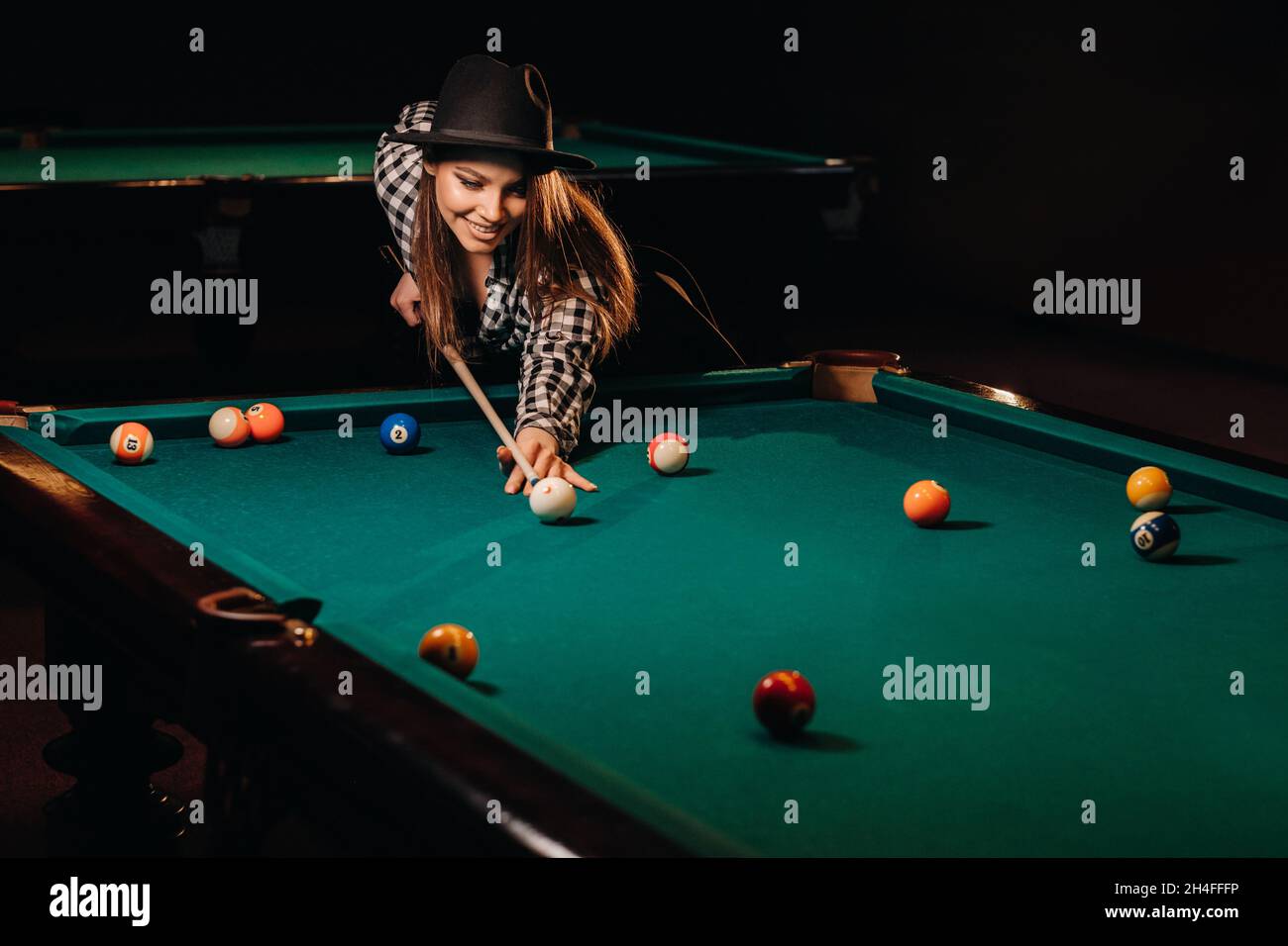 A girl in a hat in a billiard club with a cue in her hands hits a  ball.Playing pool Stock Photo - Alamy