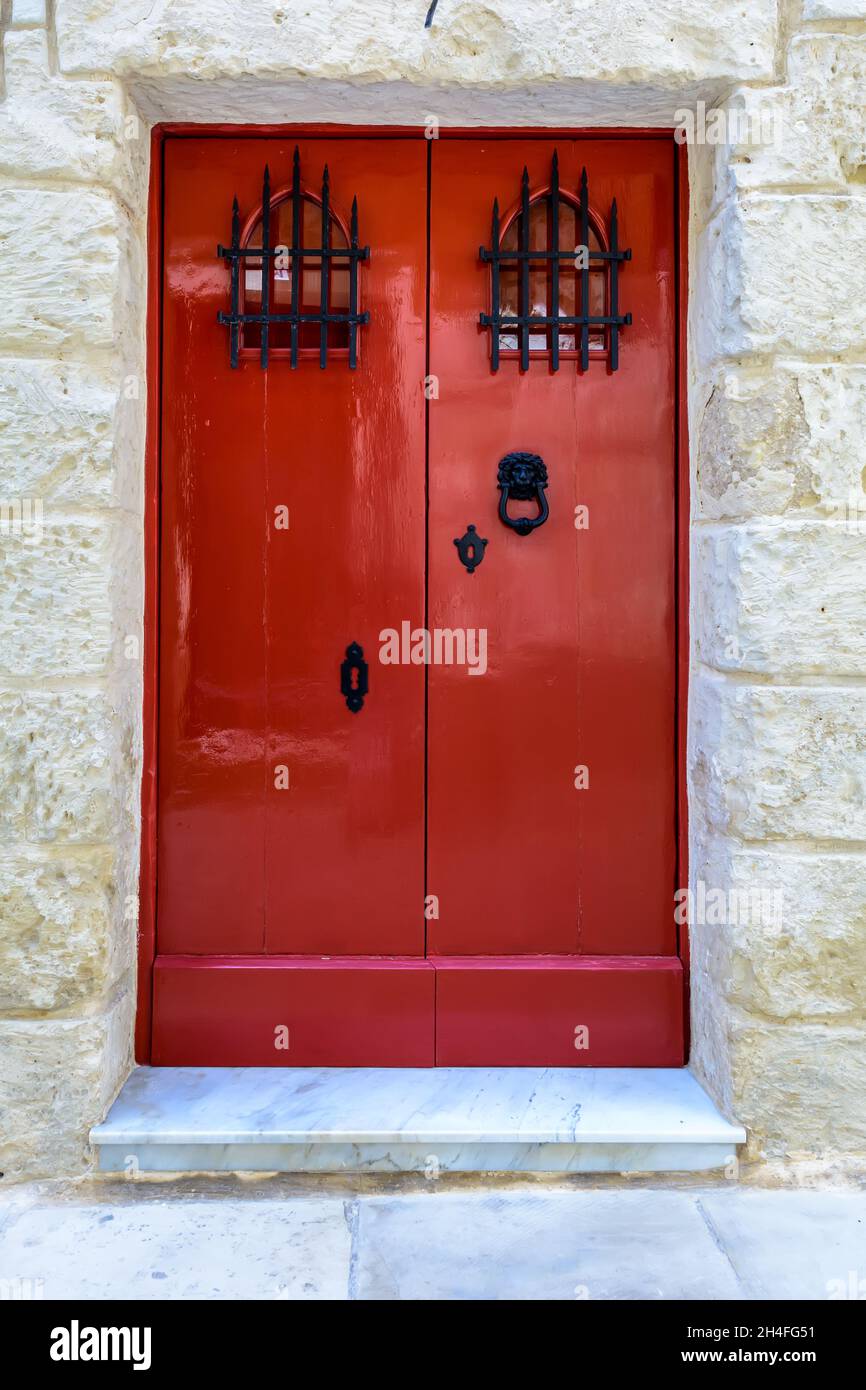 Red wooden door with black forged vintage lion head shaped ring knocker and gratings on small windows Stock Photo