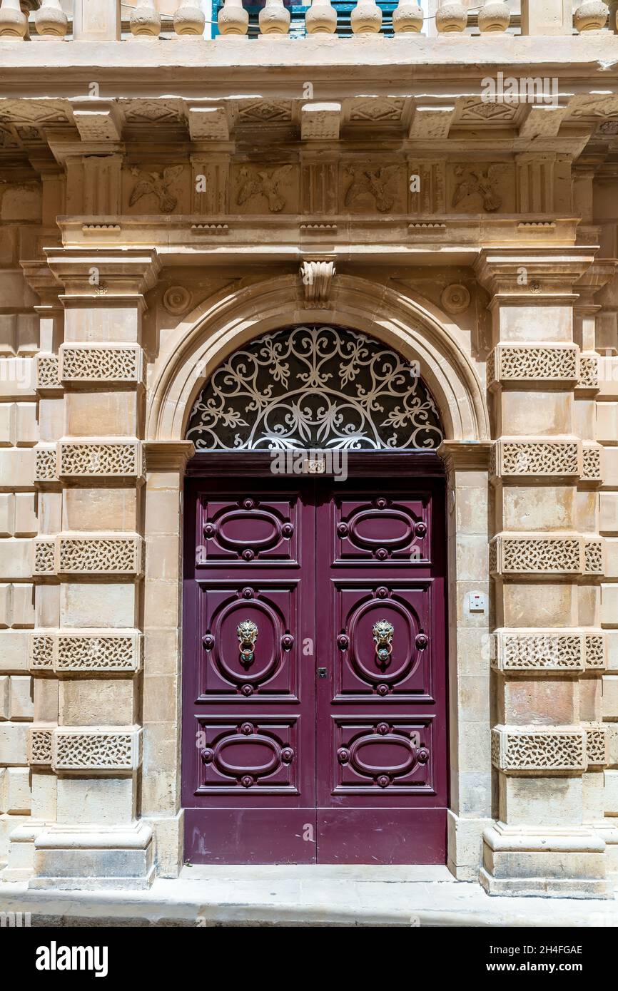 Burgundy wooden arched door decorated with gilded door knockers with lion heads. Vintage entry doors in Mdina, Malta. Stock Photo