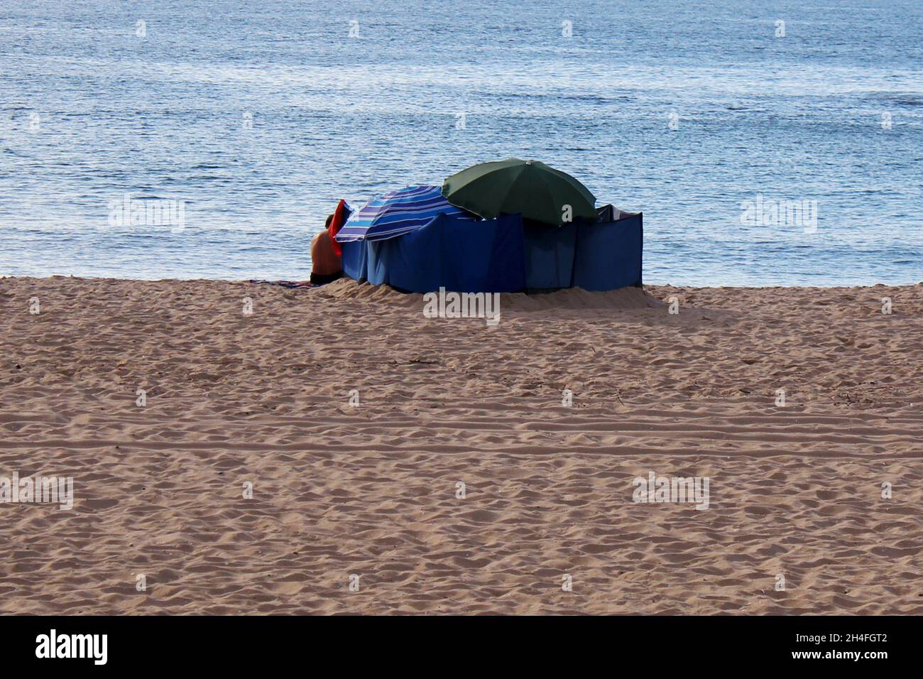 Der Rücken eines Mannes (keine Erkennbarkeit) sowie Sonnenschirme und Beach Wind Screen Windschutz am Strand von Espinho, Portugal. Stock Photo