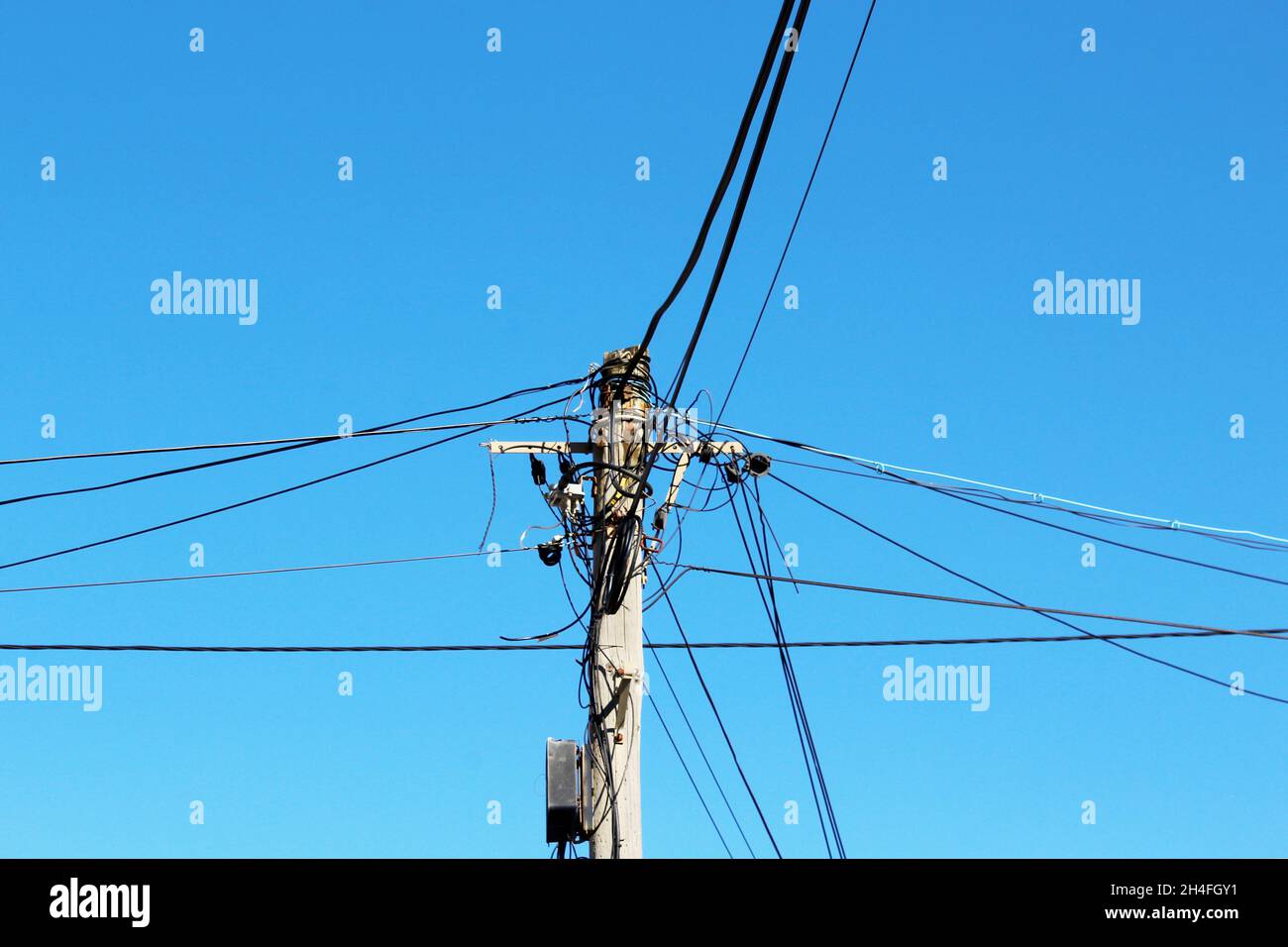 Strommasten mit vielen Stromleitungen, die um den Masten gewickelt sind, vor einem blauen, wolkenlosen Himmel in Espinho, Portugal. Stock Photo