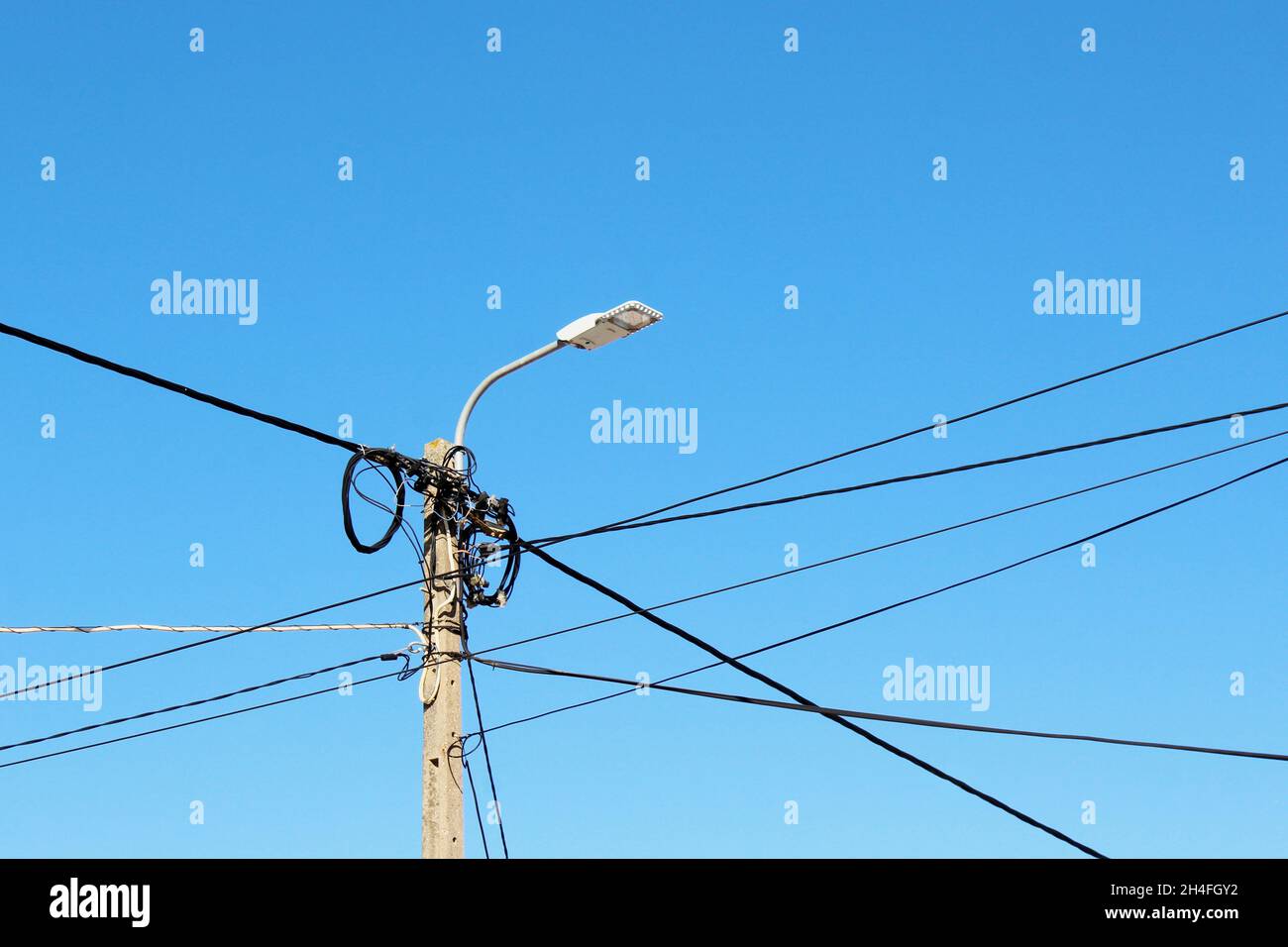 Strommasten  mit Laterne und mit vielen Stromleitungen, die um den Masten gewickelt sind, vor einem blauen, wolkenlosen Himmel in Espinho, Portugal. Stock Photo