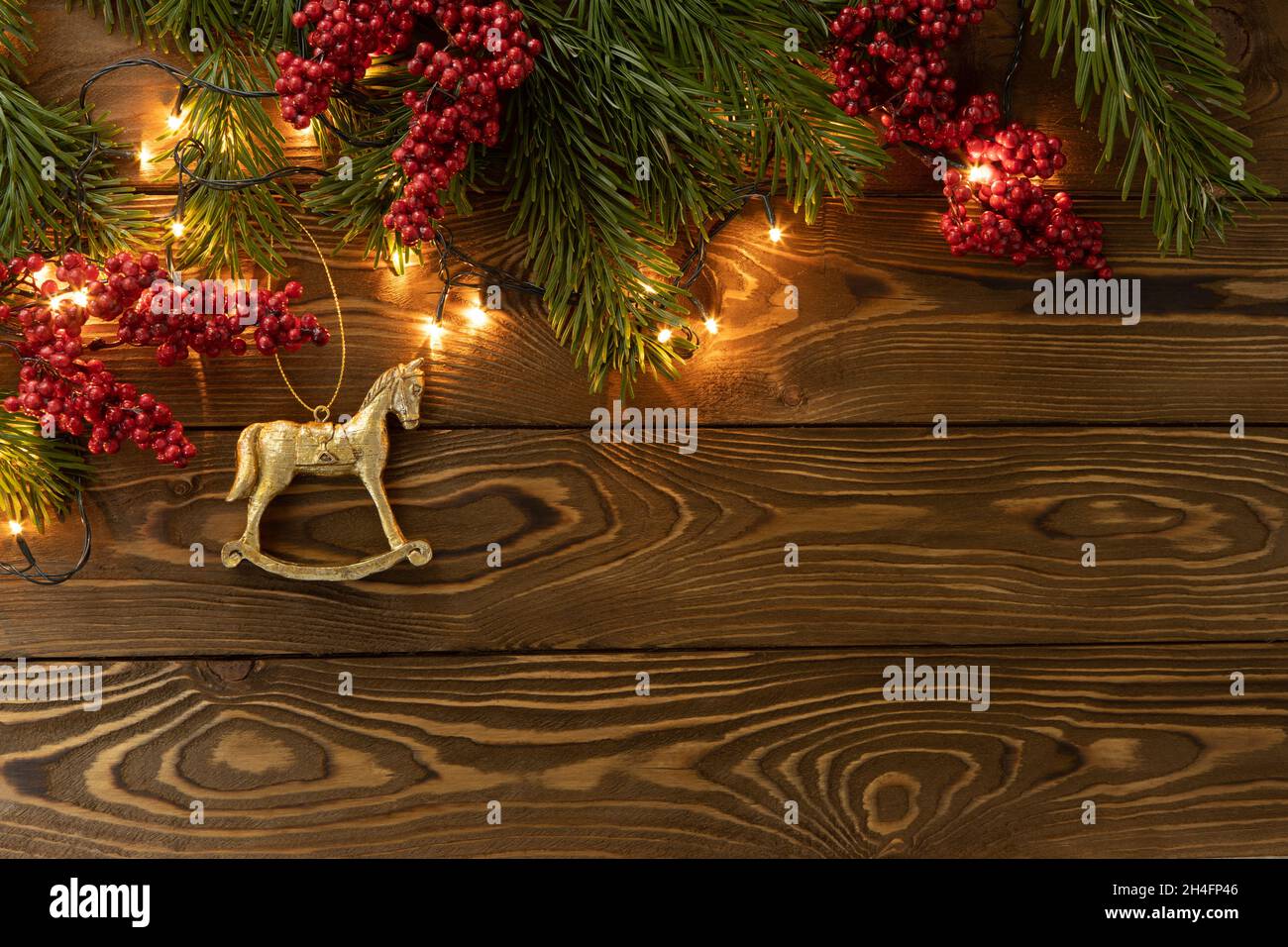 Christmas background. Nobilis fir branches, twigs with red berries, toy golden horse on brown wooden planks. Copy space, flat lay, top view. Holiday, Stock Photo